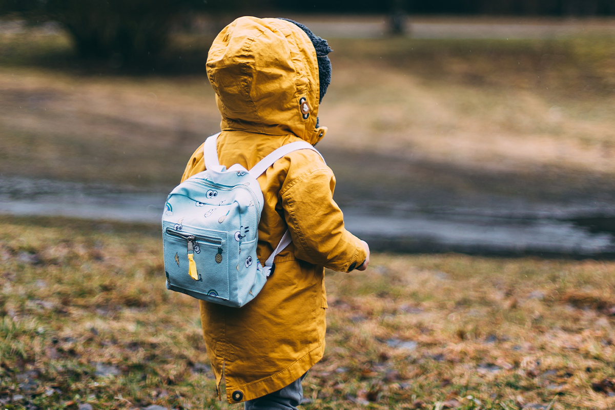 Kleinkind mit gelber Jacke und hellblauen Rucksack