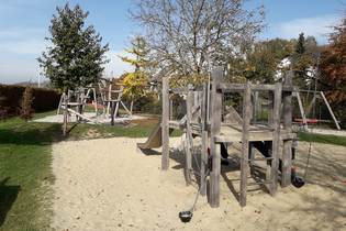 Spielplatz mit großer Sandfläche in der ein Gerüst aus Holz steht