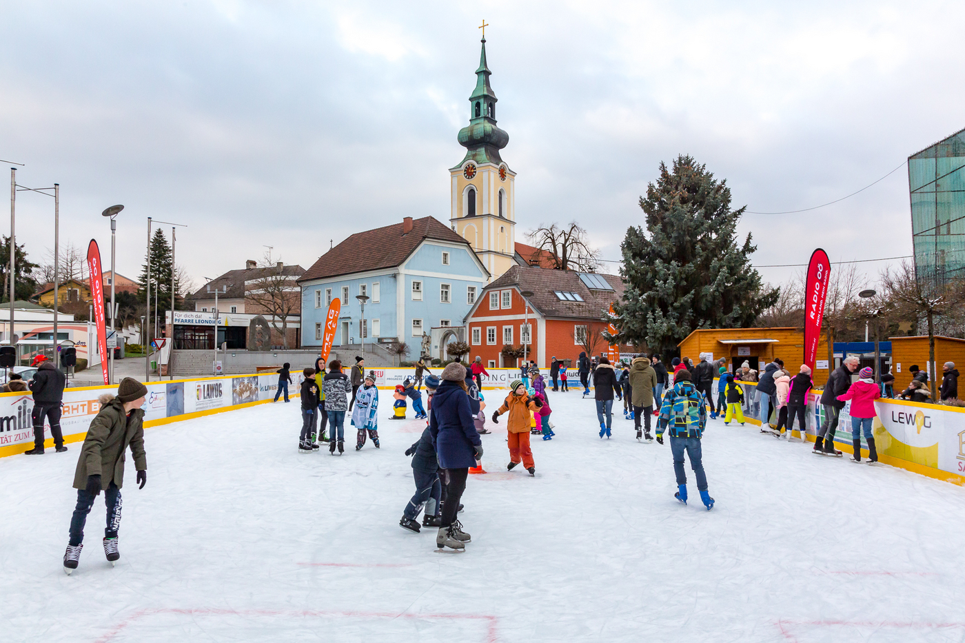 Eislaufplatz mit Kindern, Hintergrund: Kirche und blaues Haus