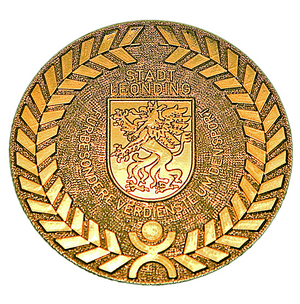 Goldene runde Medaille, in der Mitter das Wappen von Leonding mit einem Drachen  