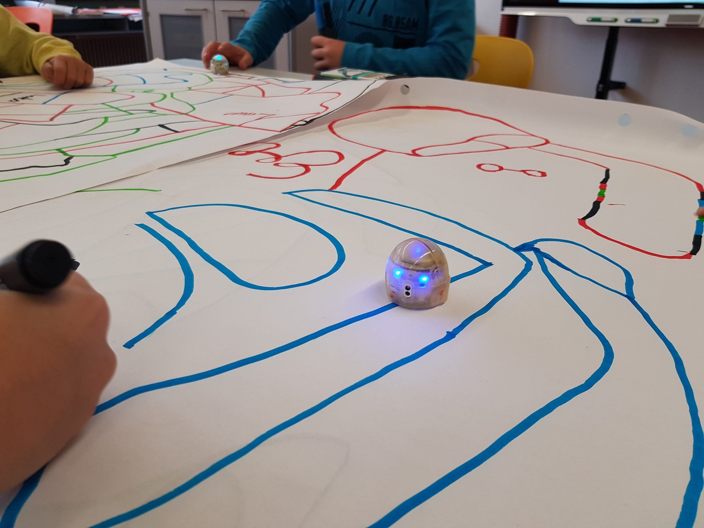 Kleiner Roboter fährt auf blauer Linie, Kinder malen die Linie